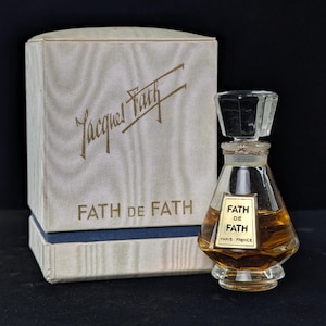 May include: Vintage perfume bottle of Fath de Fath with a clear faceted stopper and a gold label. The bottle is filled with amber-colored liquid. The box is off-white with gold lettering and the brand name.