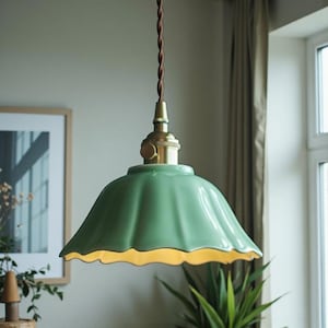 May include: A green ceramic pendant light with a scalloped edge and brass fittings. The light hangs from a brown twisted cable. The interior of the shade is a warm yellow colour.