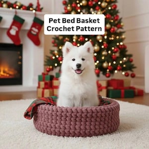 Może przedstawiać: Biały pies siedzi w koszu na łóżko dla zwierząt domowych zrobionym na szydełku w kolorze malwy. Łóżko jest okrągłe i ma gruby, teksturowany wygląd. Tekst "Pet Bed Basket Crochet Pattern" znajduje się na górze. W tle choinka i kominek.