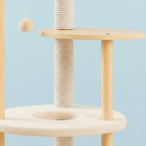 May include: A multi-level cat tree featuring light-colored wooden support posts, a central vertical post wrapped in thick white sisal rope, a circular platform with a soft cream-colored fabric cushion, and a hanging cream-colored ball toy.