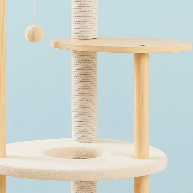 May include: A multi-level cat tree featuring light-colored wooden support posts, a central vertical post wrapped in thick white sisal rope, a circular platform with a soft cream-colored fabric cushion, and a hanging cream-colored ball toy.