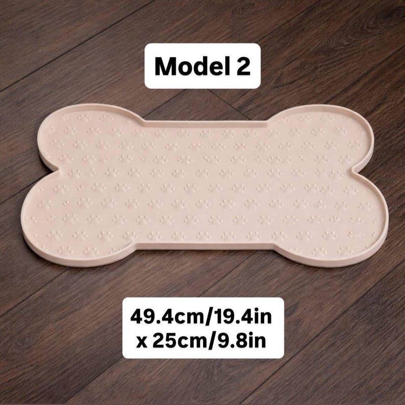 May include: A light pink, bone-shaped pet food mat with a paw print pattern. The mat is 19.4 inches long and 9.8 inches wide. The text "Model 2" is displayed on the mat.
