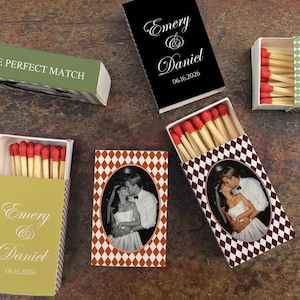 May include: Matchboxes with red-tipped matches. Some boxes feature a photo of a couple, while others have text that reads "Emery & Daniel" and the date "06.16.2026". One box reads "THE PERFECT MATCH".