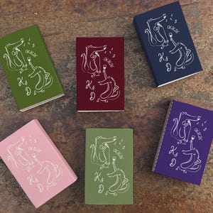 May include: Five small, rectangular boxes in various colors: green, burgundy, navy, purple, and pink. Each box features a white illustration of two alligators with a wine glass, musical notes, and the text "06.16.26" and "K & D".
