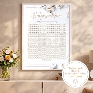 Könnte beinhalten: Ein gerahmter Hochzeits-Countdown-Kalender mit weißem Rahmen. Der Kalender zeigt ein Raster aus Herzformen, jede nummeriert, mit dem Text "Hochzeitscountdown" und "365 Tage bis zu unserem grossen Tag". Dekorative florale Akzente sind sichtbar.