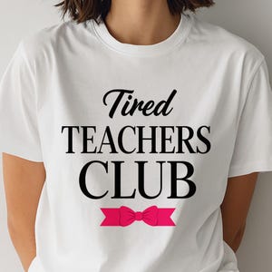 Puede incluir: Camiseta blanca con el texto negro "Tired TEACHERS CLUB" y un lazo rosa. La camiseta tiene cuello redondo y mangas cortas.