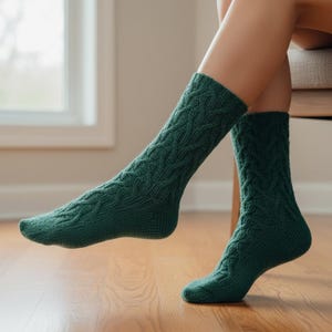 May include: A pair of dark green cable knit socks. The socks are knee-high and have a textured pattern. The socks are worn by a person sitting on a chair, with their feet resting on a wooden floor.