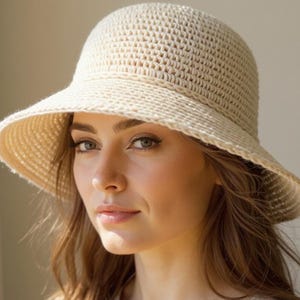 May include: A cream-colored, crocheted sun hat with a wide brim and a rounded crown. The hat is made of a textured, open-weave material, perfect for sun protection. The hat is a stylish accessory for outdoor activities.