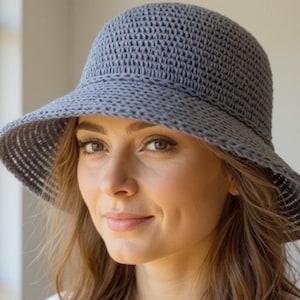 May include: A gray, woven sun hat with a wide brim. The hat has a structured crown and a slightly curved brim. The hat is made of a textured material and appears to be lightweight. The hat is designed to provide shade from the sun.