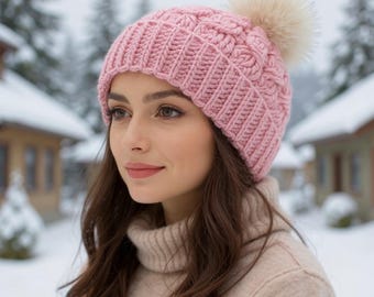May include: A pink knitted beanie with a cable knit design and a fluffy, cream-colored pom-pom. The hat is made of a soft material and is suitable for cold weather. The beanie is a stylish accessory.
