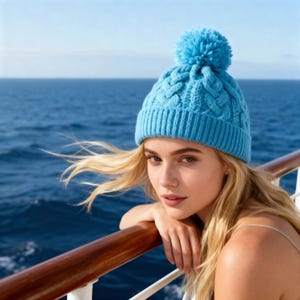 Puede incluir: Un gorro de punto trenzado azul claro con un pompón a juego. El gorro tiene un borde acanalado y un patrón tejido texturizado. El gorro es de un tono azul vibrante, perfecto para el clima frío.
