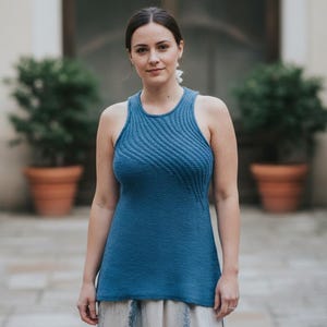 May include: A blue tank top with a textured, wave-like pattern on the front. The sleeveless top has a round neckline and a slightly flared hem. The background features potted plants and a stone walkway.