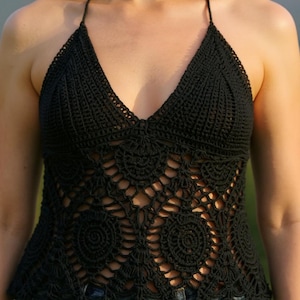 May include: Black crochet halter top with a deep V-neck and detailed openwork. The top has a halter neck tie and a fitted shape, with a floral pattern. The garment is made of a dark, solid-colored yarn, perfect for summer wear.