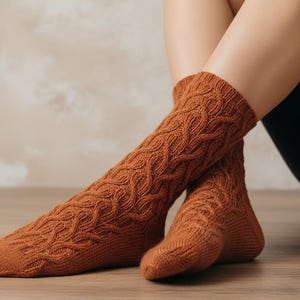 May include: A pair of rust-colored knitted socks with a cable knit pattern. The socks are knee-high and have a textured design. The socks are displayed on a person's legs, with one leg extended and the other bent.
