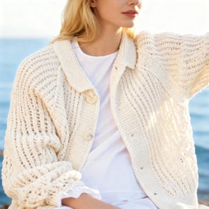 May include: Cream-colored, open-weave cardigan with a collared neckline and button closure. The knitted sweater features a textured design and is paired with a white top. The sleeves have a unique, open-weave pattern. The cardigan is a cozy, stylish garment.