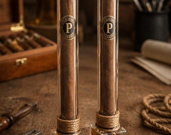 May include: Two brown cigars, each encased in a vertical glass tube with a cork stopper. The base of each tube is a square glass vessel filled with amber liquid, wrapped in twine. A label on each base reads Handmade in France.