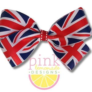 May include: A handmade hair bow featuring the Union Jack flag design in red, white, and blue. The bow is made of ribbon and has a stitched center. The text "pink lemonade DESIGNS" is visible on the bottom of the bow.