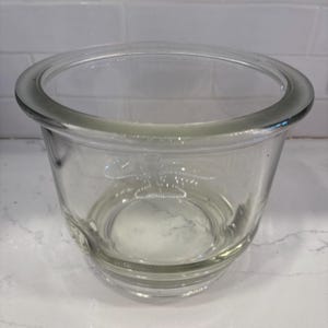 May include: A clear glass bowl with a rounded rim and a slightly tapered body. The bowl is transparent, allowing a view of the interior. The design is simple and functional, suitable for various uses.