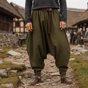 May include: Olive green harem trousers with a brown leather belt and matching shoes. The trousers have a loose, baggy fit with fitted ankles. The belt is fastened with a simple buckle. The shoes are brown leather with decorative studs.