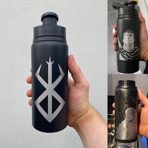 May include: Black water bottles with silver designs. One bottle has a symbol, another features a manga character, and the third has a different manga character. The bottles have black lids and are held by a person.