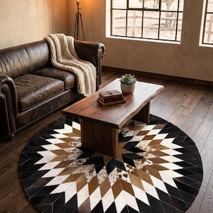 Peut inclure: Un tapis rond avec un motif géométrique dans les tons de noir, blanc, marron et beige. Le tapis est en peau de vache et est posé sur un parquet. Une table basse en bois et un canapé en cuir sont visibles en arrière-plan.