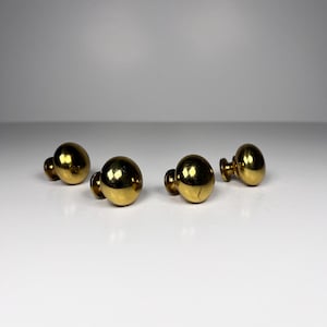 Può includere: Quattro pomelli per mobili in ottone dalla forma rotonda e sferica. I pomelli hanno una superficie lucida e riflettente e una piccola base cilindrica. Sono disposti su una superficie bianca.