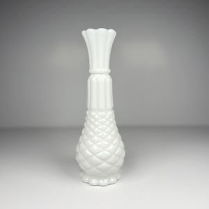 May include: A tall, opaque white milk glass bud vase featuring a flared, scalloped rim, a slender neck with vertical fluting, and a bulbous base decorated with a raised, diamond-shaped lattice pattern that terminates in a scalloped bottom edge.