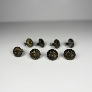 Peut inclure: Dix boutons de meuble anciens en laiton. Chaque bouton présente un design rond et cannelé avec une finition sombre et vieillie. Les boutons sont disposés sur une surface blanche, mettant en valeur leur esthétique vintage. Idéal pour la restauration de meubles.