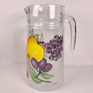 May include: A clear glass jug with a handle and spout, decorated with fruit illustrations. The design includes a yellow pear, purple grapes, and green leaves. The word "FRANCE" is printed on the jug.