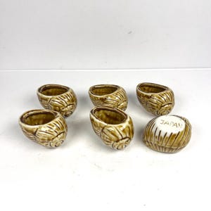Peut inclure: Ensemble de six porte-œufs en céramique de couleur marron. Les supports présentent un motif texturé et strié. L'un des supports porte l'inscription "JAPAN". Ces supports décoratifs sont parfaits pour les petits objets.