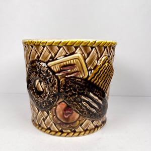 Peut inclure: Pot de fleurs en céramique avec un motif de panier tressé dans les tons marron et beige. Le pot présente des outils de barbier en relief, dont un rasoir, un peigne et une fleur. Le bord est orné d'un motif de corde jaune.