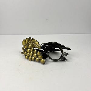 Peut inclure: Deux ronds de serviette en métal. L'un représente une grappe de raisins dorés avec une feuille, l'autre est de couleur bronze foncé. Les ronds de serviette sont conçus pour maintenir les serviettes en tissu et ajouter une touche décorative.