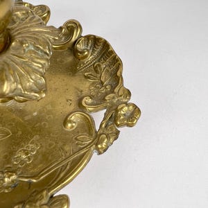 May include: Close-up of a brass decorative object with floral and leaf motifs. The object has an ornate design with intricate details, including flowers and leaves. The brass has a warm, golden hue.