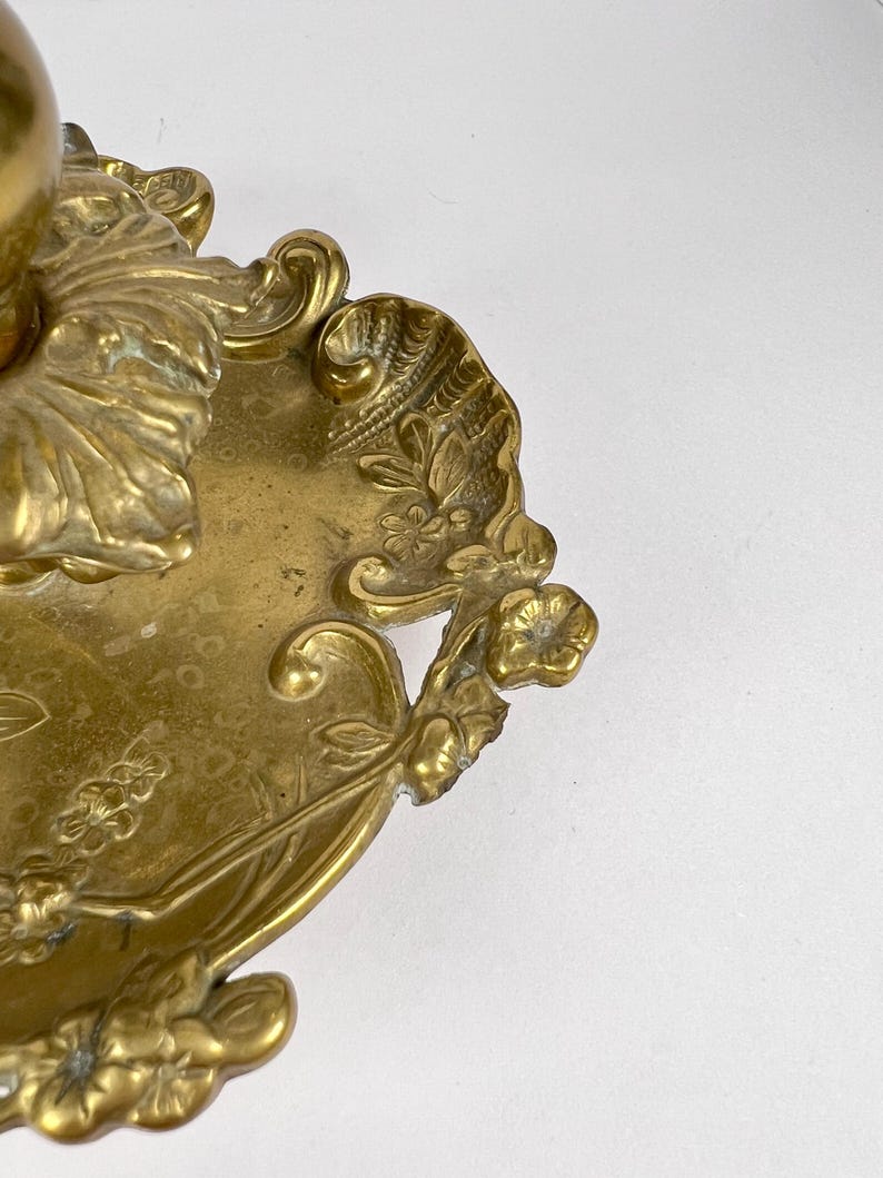 May include: Close-up of a brass decorative object with floral and leaf motifs. The object has an ornate design with intricate details, including flowers and leaves. The brass has a warm, golden hue.