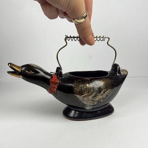 Peut inclure: Une saucière ou crémier vintage en céramique en forme de canard. Le corps brun foncé présente des accents dorés et un nœud rouge. Il est doté d'un bec doré et d'une poignée en métal. Le crémier repose sur une base arrondie.