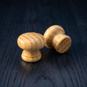 May include: Two light-colored wooden cabinet knobs with a smooth, polished finish and visible natural grain patterns. Each knob features a rounded top and a tapered base, showcasing the warm, tan hues of the wood material in a set of two.