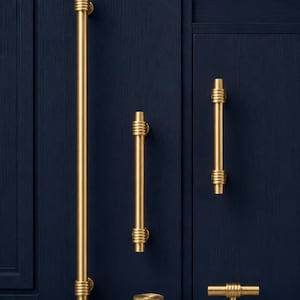 Könnte beinhalten: Eine Sammlung goldfarbener Schrankbeschläge vor einem dunkelblauen Hintergrund. Das Set umfasst verschiedene Größen von Stangengriffen, einen Knauf und einen T-Griff, alle mit geripptem Design. Die Beschläge sind wahrscheinlich für Küchen- oder Badezimmerschränke.