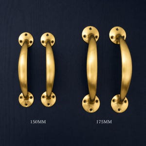 Könnte beinhalten: Vier Messing-Türgriffe mit gebogenem Design, montiert auf kreisförmigen Platten mit Schraubenlöchern. Zwei Sätze sind abgebildet, einer mit der Aufschrift 150MM und der andere mit 175MM, vor einem dunkelblauen Hintergrund. Die Griffe haben eine polierte Oberfläche.