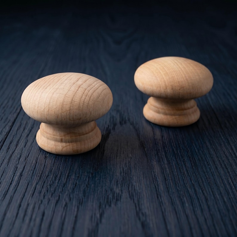 Puede incluir: Dos pomos redondos de madera clara con un acabado suave y veta natural. Cada pomo presenta una parte superior ancha en forma de seta y una base circular escalonada, mostrando la textura org&aacute;nica y el color tostado claro de la madera.
