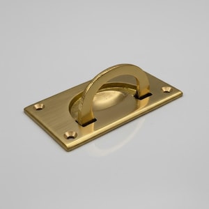May include: A rectangular brass flush pull with a curved handle. The handle is raised and textured, and the base has rounded corners with screw holes. The hardware has a polished finish.