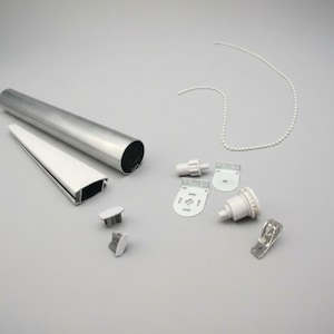 May include: A selection of window blind parts, featuring a silver metal roller tube, a white plastic valance, several white plastic brackets, and a beaded chain. The components are displayed on a light grey surface.