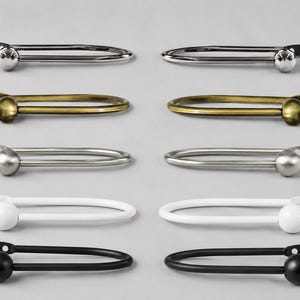 Peut inclure: Un ensemble de dix embrasses à rideaux en métal en forme de U disposées par paires, chacune dotée d'un embout sphérique et d'une plaque de fixation plate avec deux trous de vis. La collection comprend des finitions chrome, laiton, nickel, blanc et noir.