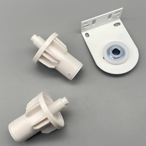 May include: White roller shade hardware components. The image shows two cylindrical pieces with a ridged wheel and a mounting bracket with a roller bearing. The components are made of white plastic and metal.