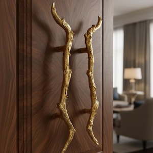 May include: A pair of gold-colored, branch-shaped cabinet handles mounted on a dark wood cabinet door. The handles have a textured, organic design, adding a touch of nature-inspired elegance to the furniture.