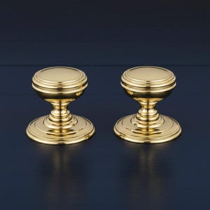 May include: Two polished brass cabinet knobs featuring a rounded top, a tiered neck, and a wide circular base. The hardware has a reflective metallic finish with concentric ring details on the top and the base, creating a uniform appearance.