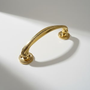 May include: A curved, brass-coloured door pull with a rope-like design along the handle. The pull has decorative circular bases at each end, adding a classic touch. The hardware is designed for easy installation and adds a touch of elegance.