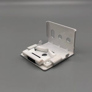 May include: A white, right-angled bracket with a series of holes and slots. The bracket has a flat base with several raised, rectangular features and a black insert. The object is likely a hardware component.