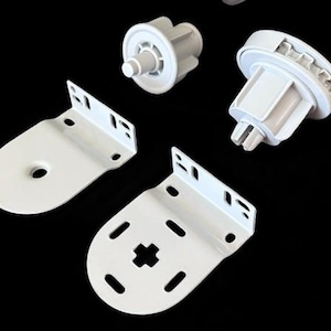 May include: White roller shade hardware components, including brackets and roller mechanisms, are arranged against a black background. The brackets have mounting holes, and the mechanisms have gears and cylindrical shapes. These parts are for window treatments.