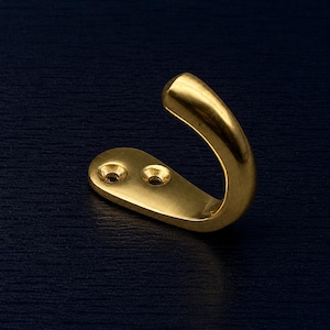 May include: A brass-coloured wall hook with a curved hook and a flat base with two screw holes. The hook is made of a shiny, metallic material and is set against a dark blue background. This hook is suitable for hanging items.