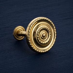 May include: A gold-colored curtain tieback with a circular design. The tieback features a decorative rope-like border and concentric circles, creating a classic and elegant look. The hardware is made of metal and has a polished finish.